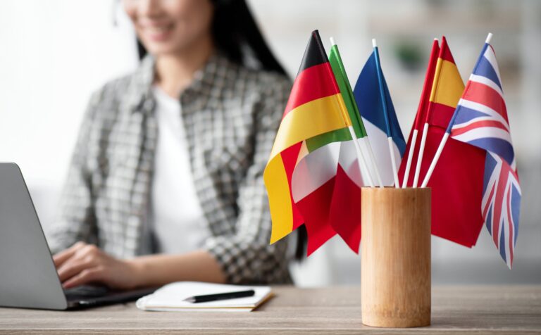 kobieta za biurkiem a przy niej zestaw flag różnych państw
